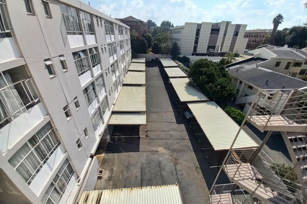 Elevated view of the apartment complex exterior, featuring a paved parking area with covered carports and external stairwell access.