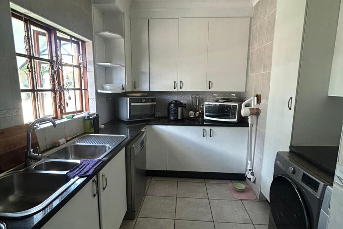 A functional kitchen featuring white cabinetry, dark countertops, a double stainless steel sink, and tiled flooring with integrated laundry appliance space.