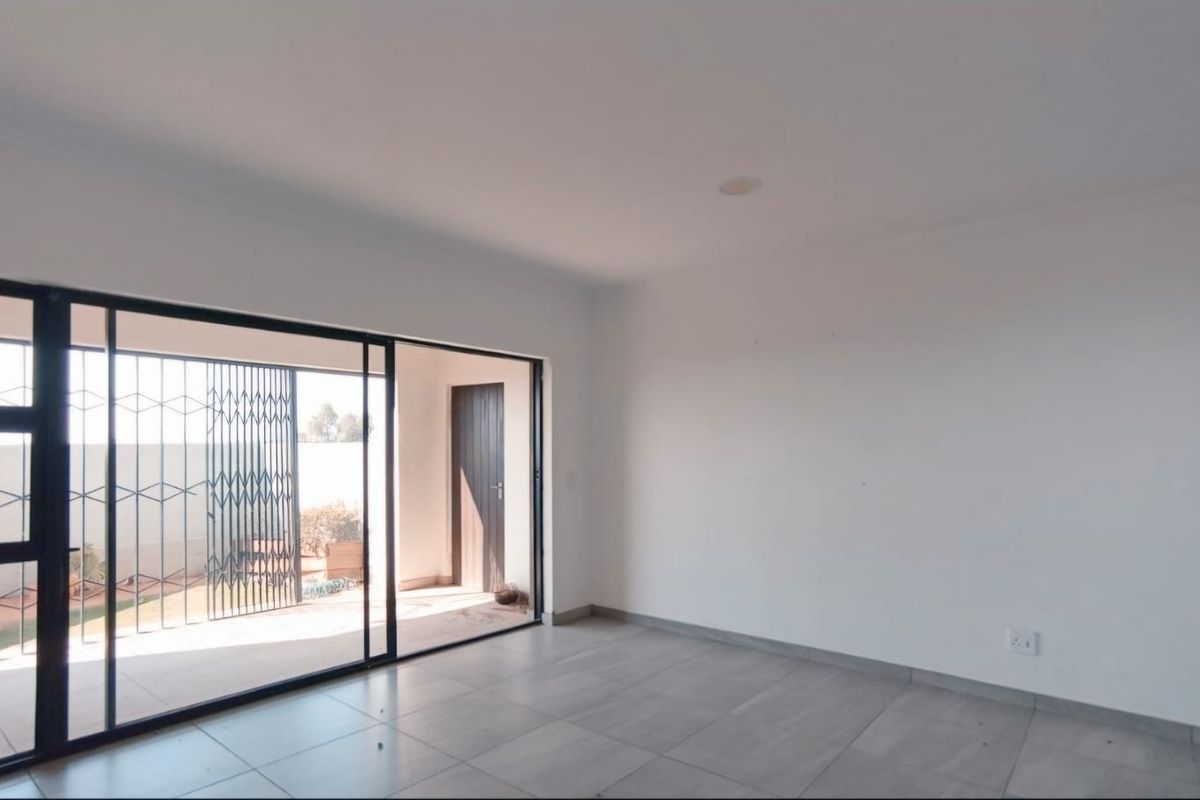 A bright, empty living area featuring large sliding glass doors that open onto a covered patio with security gates.