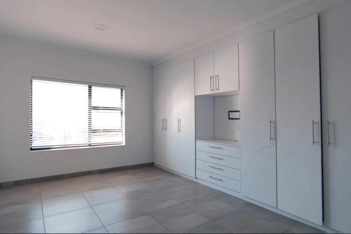 A bright, modern bedroom featuring extensive built-in cabinetry with integrated drawers and neutral floor tiling.