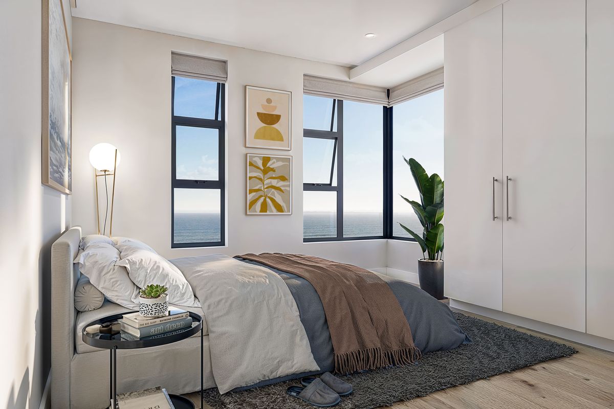 Modern bedroom featuring built-in wardrobes, timber flooring, and large windows offering expansive ocean views.