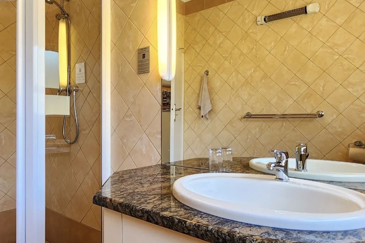 A functional bathroom featuring a shower enclosure, vanity with a granite-style countertop, integrated basin, and wall-mounted lighting.