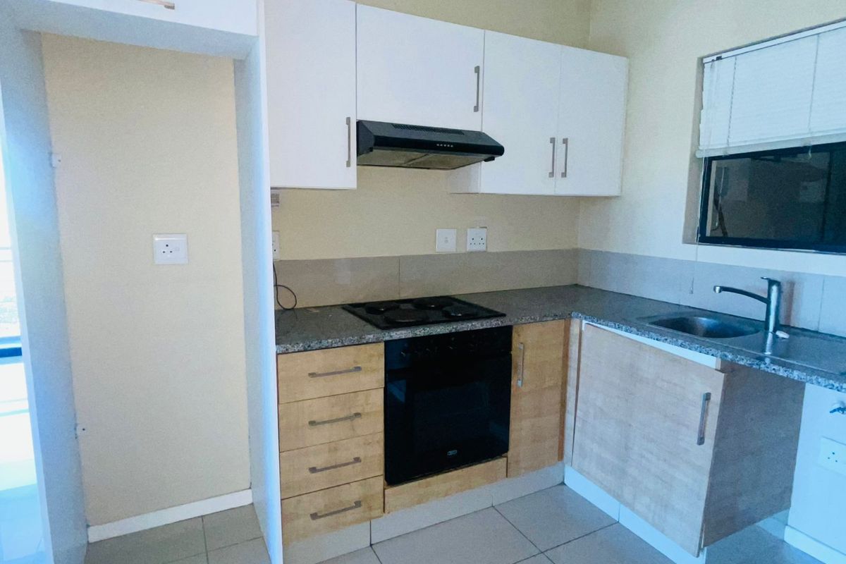 Compact kitchen featuring light wood-tone lower cabinetry, white upper cupboards, granite-look countertops, built-in oven, hob, and extractor fan.