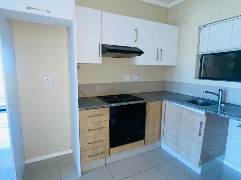 Compact kitchen featuring light wood-tone lower cabinetry, white upper cupboards, granite-look countertops, built-in oven, hob, and extractor fan.