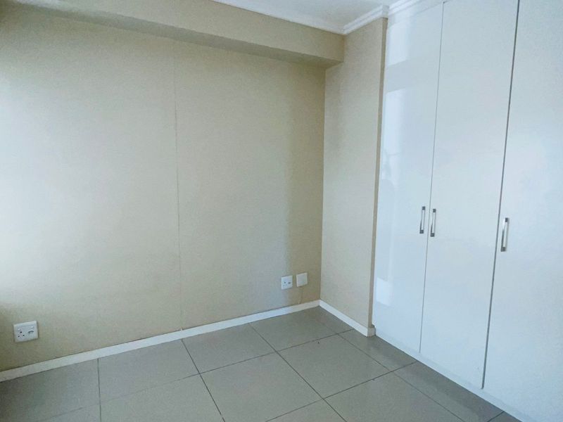 A clean, empty bedroom featuring neutral tiled flooring and built-in white cabinetry with modern handles.
