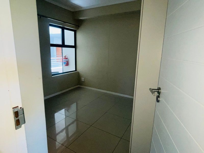 A compact, empty bedroom featuring neutral wall tones, large format floor tiles, and a window providing natural light.