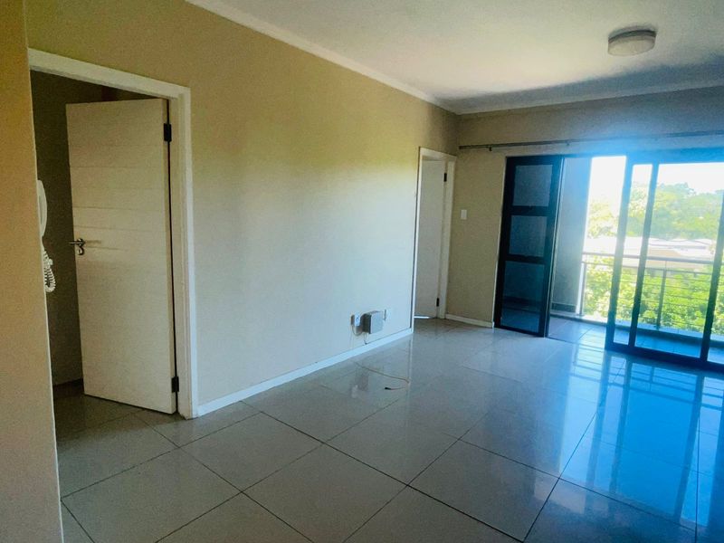 A bright, open-plan living area featuring neutral tiled flooring, access to a private balcony, and multiple doorways leading to adjacent rooms.