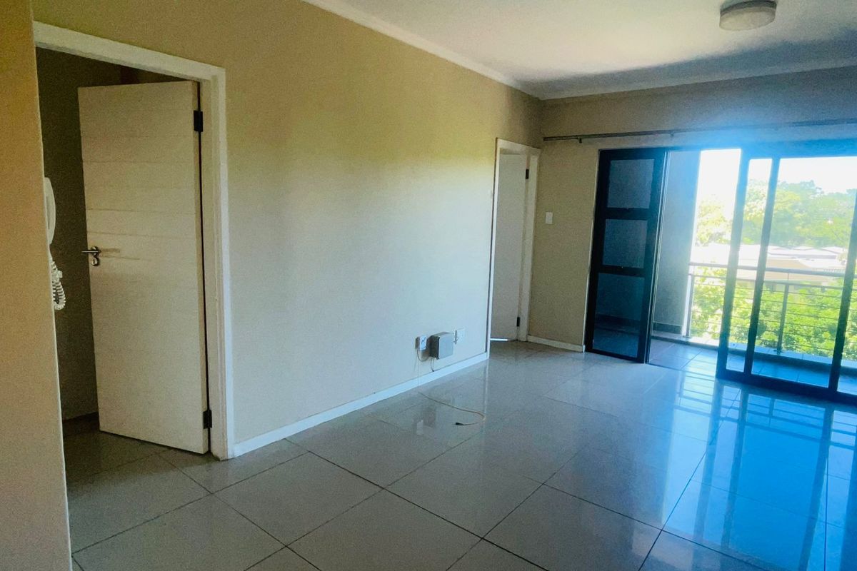 A bright, open-plan living area featuring neutral tiled flooring, access to a private balcony, and multiple doorways leading to adjacent rooms.