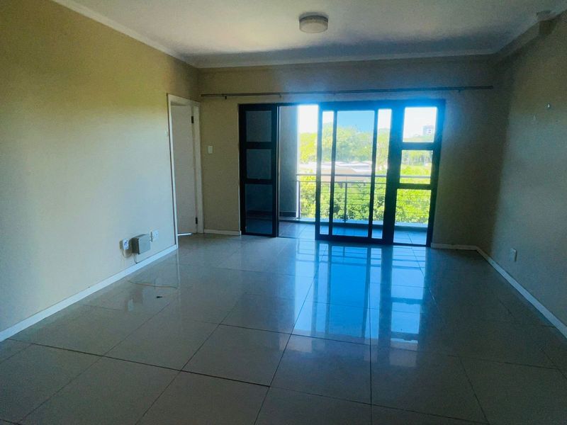 Spacious open-plan living area featuring large porcelain floor tiles and sliding glass doors that open onto a private balcony with natural light.
