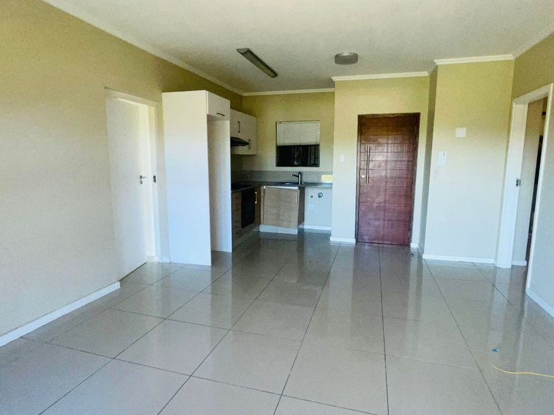 Open plan living area featuring tiled flooring and a compact kitchen with built-in cabinetry, oven, and sink.