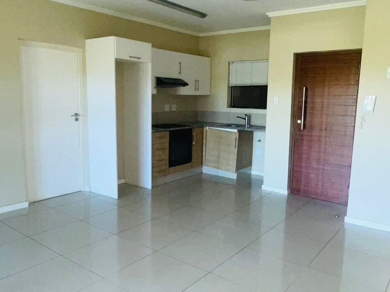 Open plan kitchen featuring built-in cabinetry, oven, hob, and extractor fan, set within a tiled living area with a wooden entrance door.