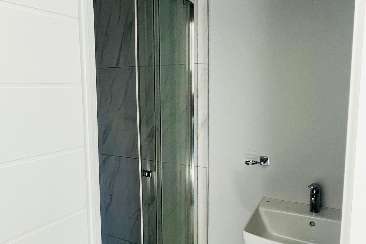 A compact bathroom featuring a glass-enclosed shower with marble-look wall tiles and a wall-mounted pedestal basin.