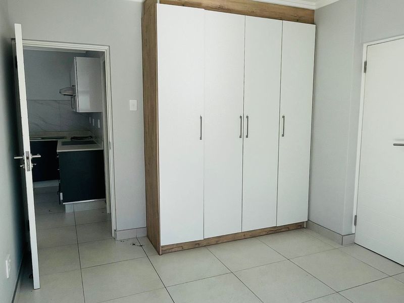 A bright bedroom featuring large format floor tiles and a modern, built-in floor-to-ceiling wardrobe with a clean white and wood-grain finish.