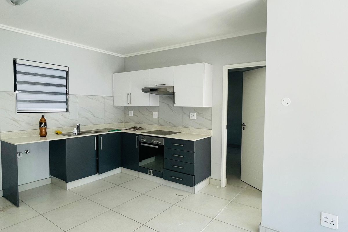 Modern kitchen featuring two-tone cabinetry, stone-look backsplash, built-in oven, hob, and extractor fan with tiled flooring.