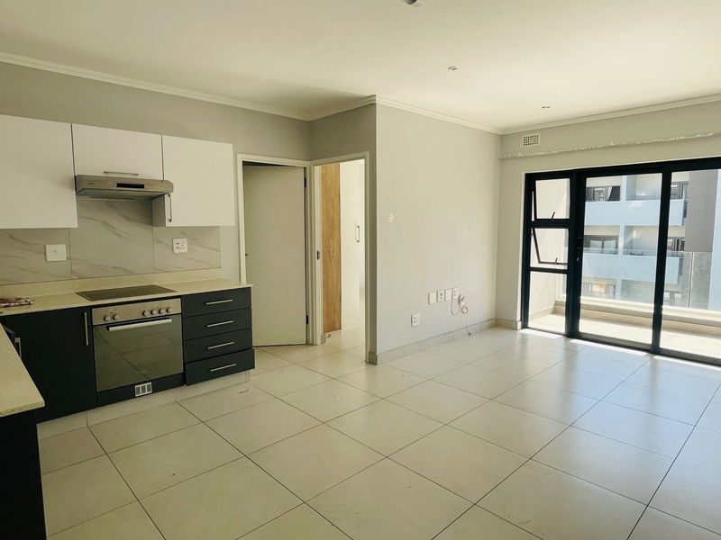 Modern open-plan kitchen and living area featuring tiled flooring, built-in cabinetry, integrated oven and hob, and sliding glass doors leading to a balcony.