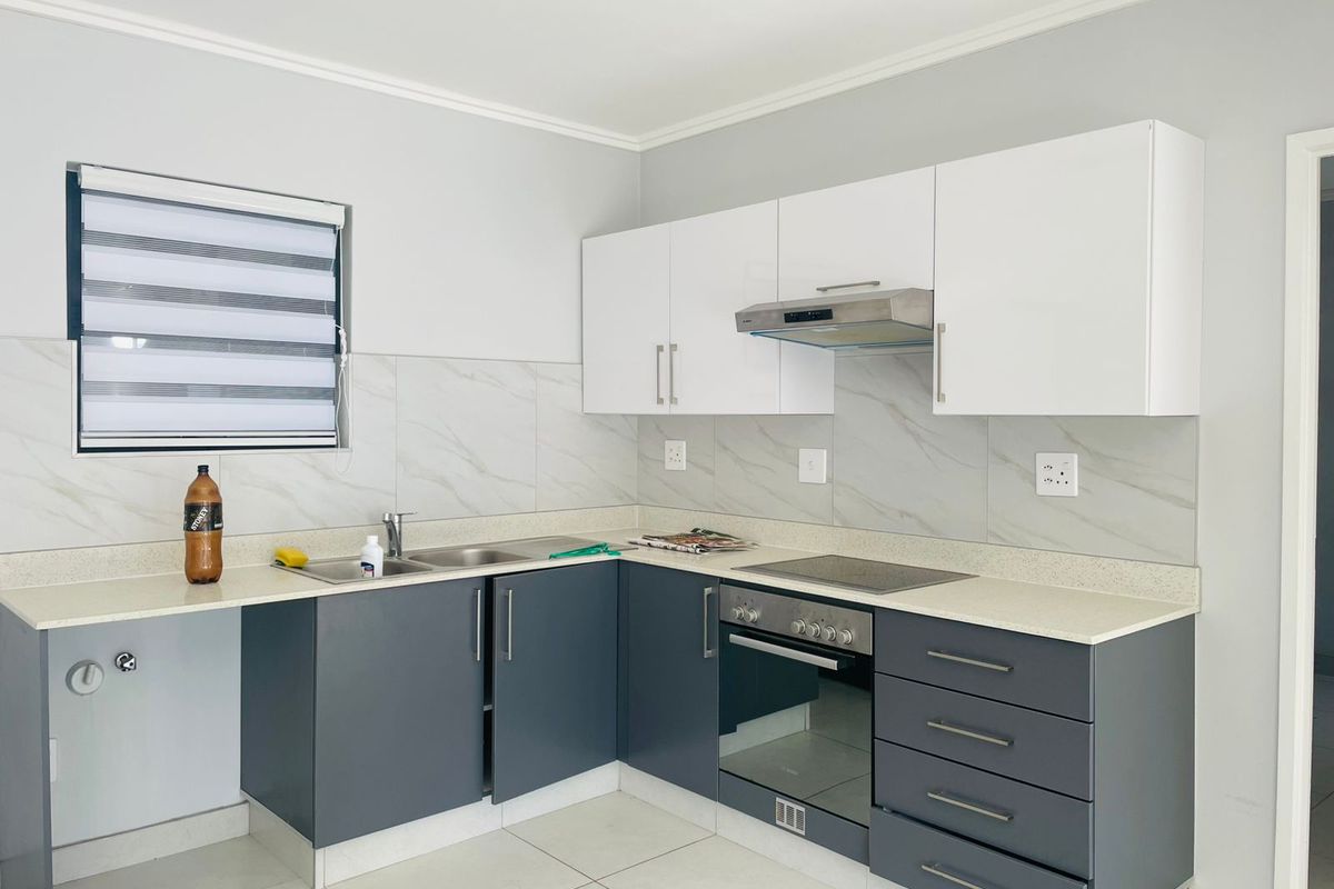 Modern kitchen featuring two-tone cabinetry, stone-look countertops, integrated oven, hob, and extractor fan with tiled splashbacks and neutral floor tiles.
