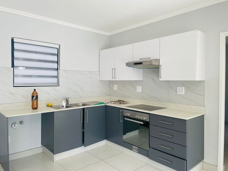 Modern kitchen featuring two-tone cabinetry, stone-look countertops, integrated oven, hob, and extractor fan with tiled splashbacks and neutral floor tiles.
