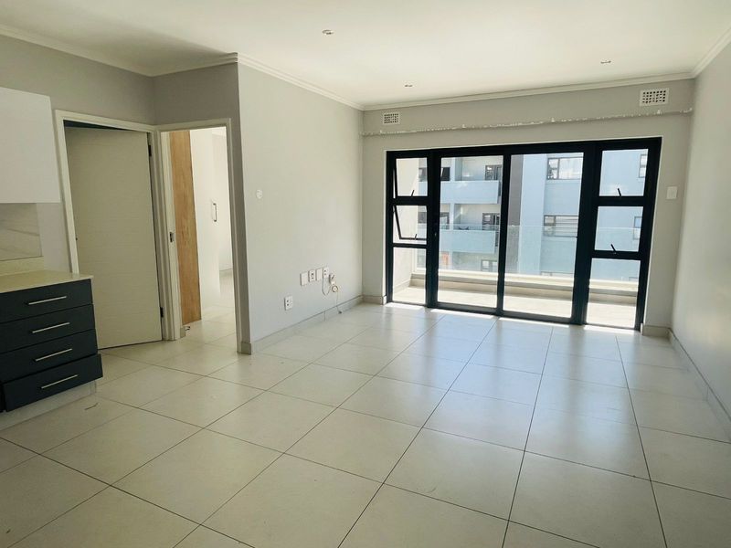 An open-plan living area featuring large sliding glass doors leading to a balcony, tiled flooring, and neutral finishes throughout.