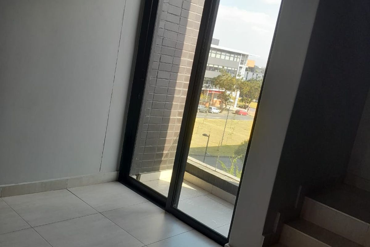 An empty living area featuring large sliding glass doors that open onto a balcony, with tiled flooring and a staircase leading to another level.