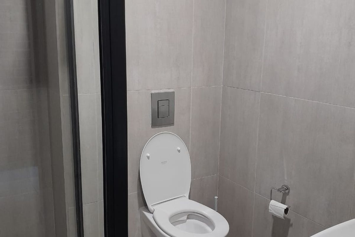 Modern bathroom featuring a wall-mounted toilet with concealed cistern, glass-enclosed shower, and neutral floor-to-ceiling tiling.
