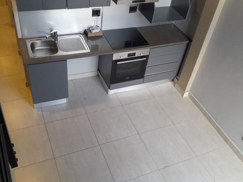 Modern compact kitchen featuring grey cabinetry, integrated oven, electric hob, extractor fan, and stainless steel sink with tiled flooring.