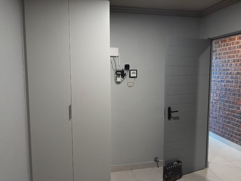 Interior view of a hallway featuring built-in cabinetry, a modern grey door, and exposed utility connections on the wall.