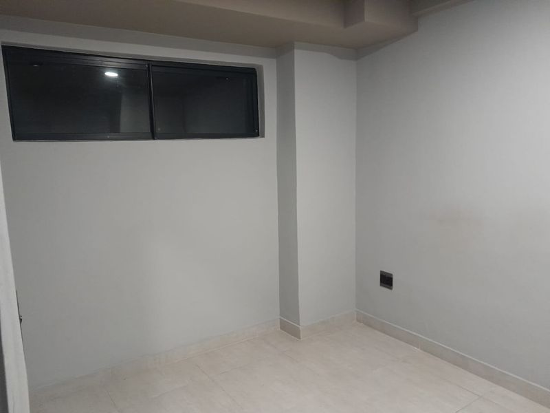 A clean, empty bedroom featuring neutral grey walls, tiled flooring, and a horizontal sliding window.