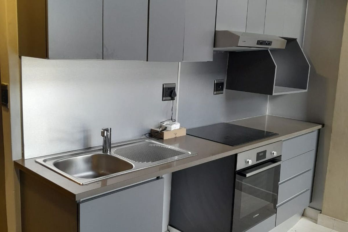 Modern compact kitchen featuring sleek grey cabinetry, integrated oven, electric hob, extractor fan, and a stainless steel sink with a metallic splashback.