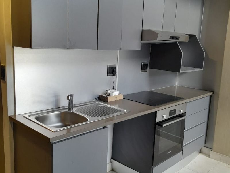 Modern compact kitchen featuring sleek grey cabinetry, integrated oven, electric hob, extractor fan, and a stainless steel sink with a metallic splashback.