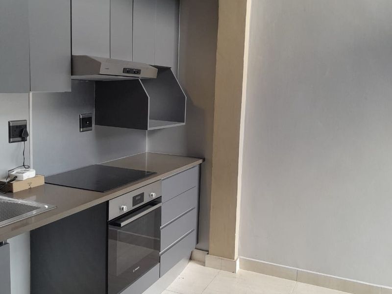 Modern kitchen featuring sleek grey cabinetry, a built-in oven, electric cooktop, extractor fan, and neutral tiled flooring.
