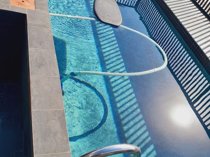 A compact swimming pool featuring tiled coping, a stainless steel ladder, and a perimeter fence, providing a private outdoor aquatic space.
