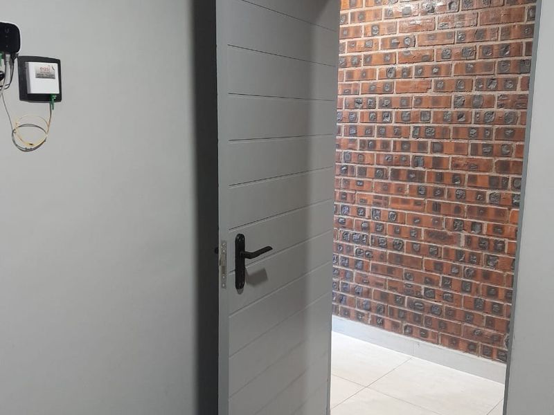 A view through a modern grey internal door into a space featuring a distinctive exposed brick feature wall and tiled flooring.