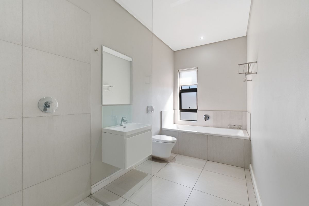 Modern bathroom featuring a wall-mounted vanity, a built-in bathtub, a glass-enclosed shower, and neutral floor-to-ceiling tiling.