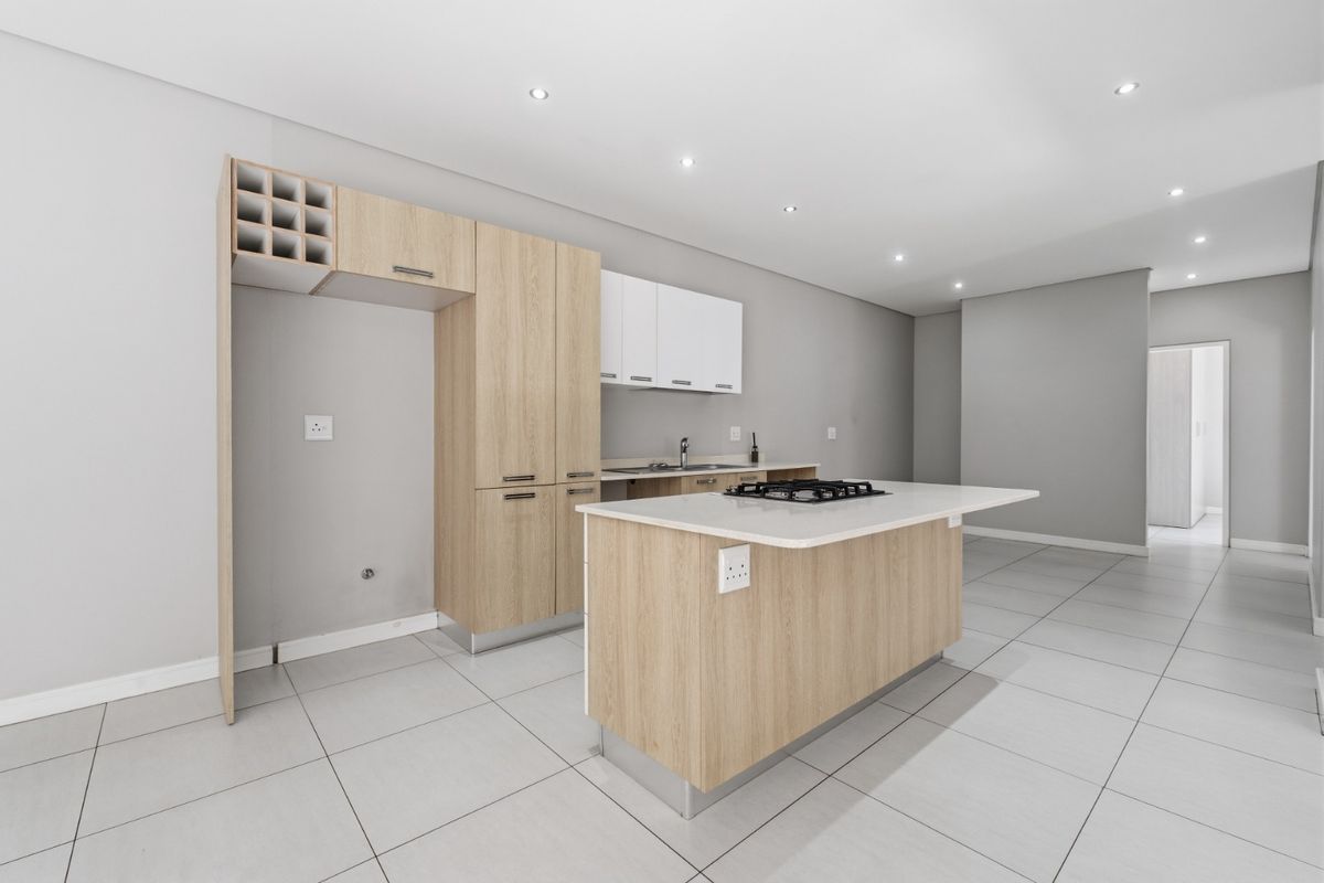 Modern open-plan kitchen featuring light wood cabinetry, a central island with a built-in gas hob, stone countertops, and recessed ceiling lighting.