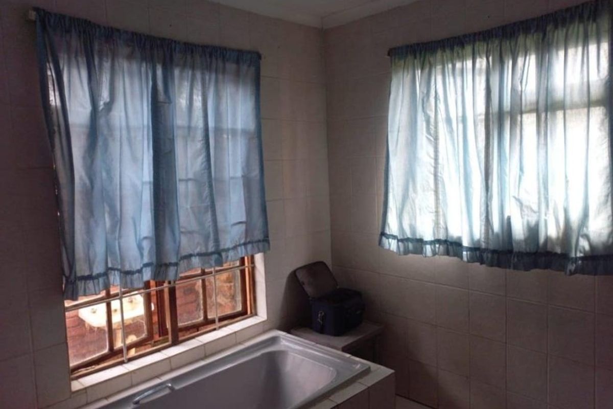 A dated bathroom featuring a built-in bathtub, tiled walls, and security bars on the windows.