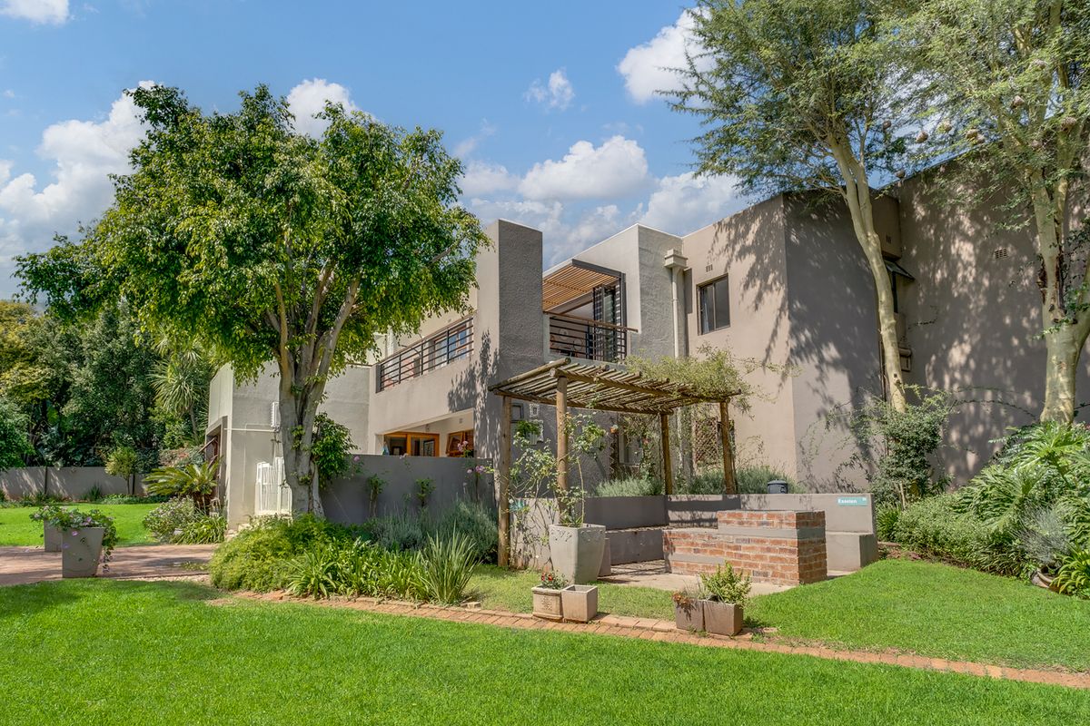 Rear view of the property featuring a landscaped garden, a brick built-in braai area with a wooden pergola, and an upper-level balcony.