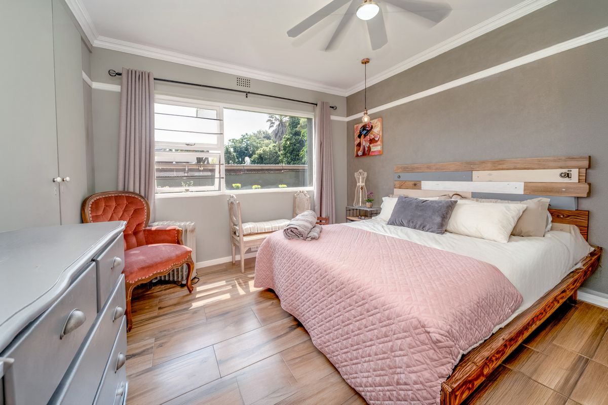 A well-maintained bedroom featuring laminate flooring, crown molding, a ceiling fan, and a built-in wardrobe, offering a comfortable and inviting living space.