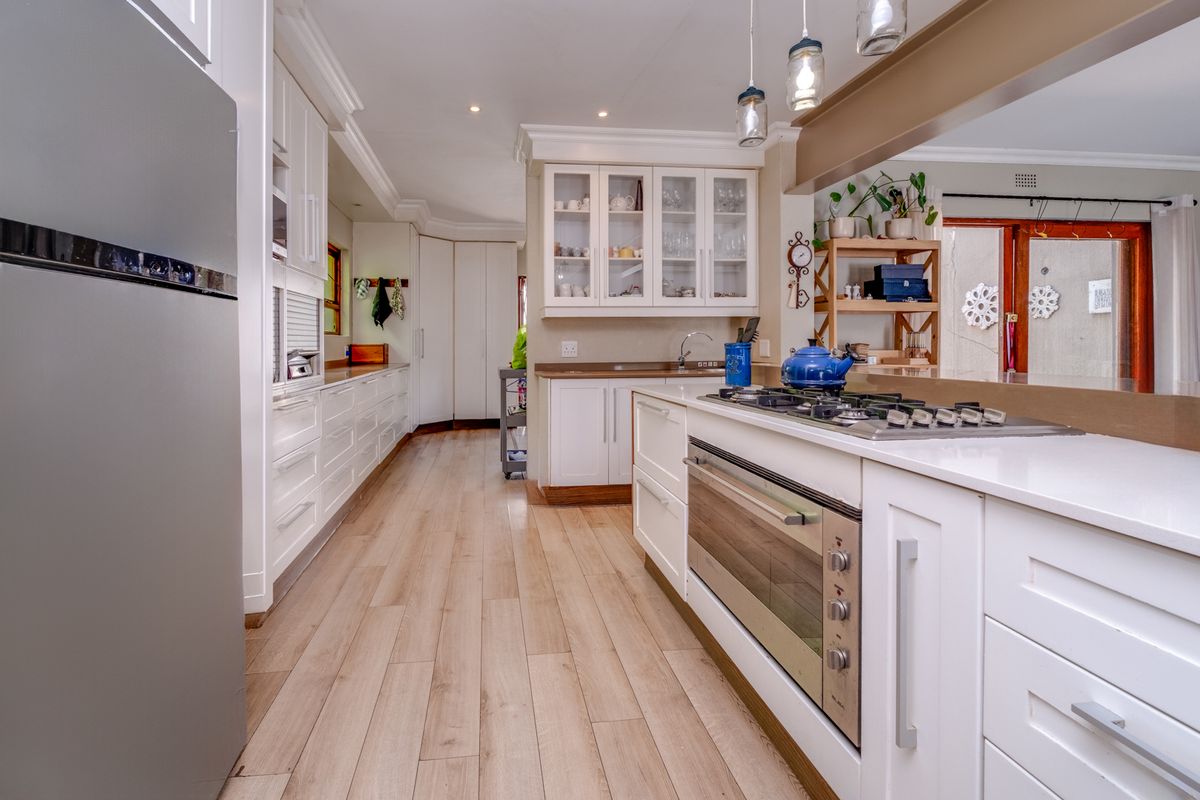 A well-appointed kitchen featuring white cabinetry, stone countertops, a built-in oven with gas hob, and modern laminate flooring with ample storage space.