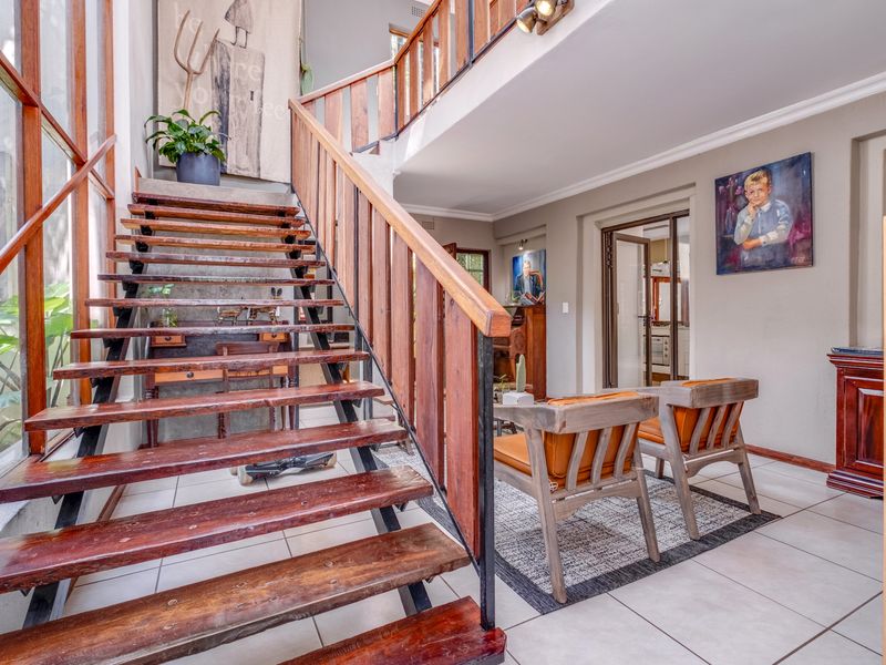 Spacious entrance hall featuring a striking open-tread timber staircase, double-volume ceiling, and tiled flooring, leading into the main living areas.