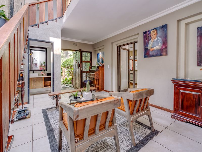 A bright living area featuring a wooden staircase, tiled flooring, and direct access to an outdoor garden space through a glass-paneled door.