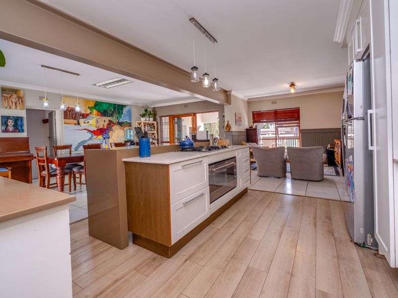 Spacious open-plan kitchen and living area featuring a central island with built-in oven, modern cabinetry, and a blend of laminate and tiled flooring.