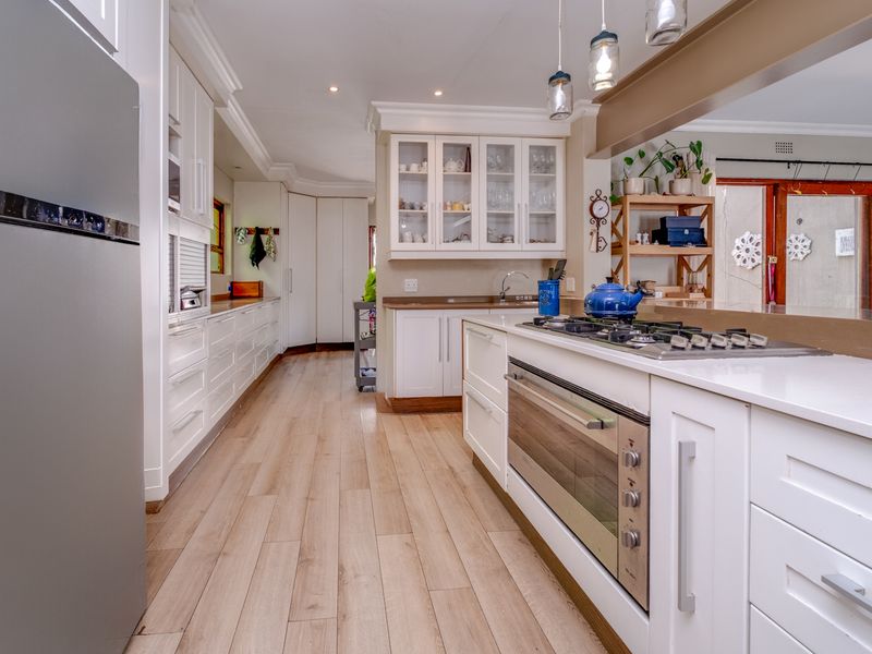 A well-appointed kitchen featuring white cabinetry, stone countertops, a built-in oven with gas hob, and modern laminate flooring with ample storage space.