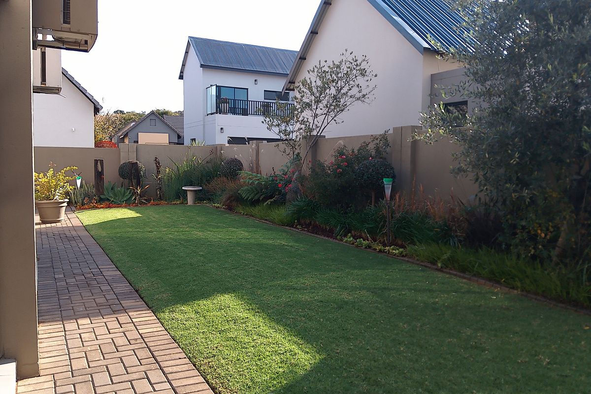 A well-maintained rear garden featuring a manicured lawn, paved walkway, and perimeter boundary wall in a residential estate setting.