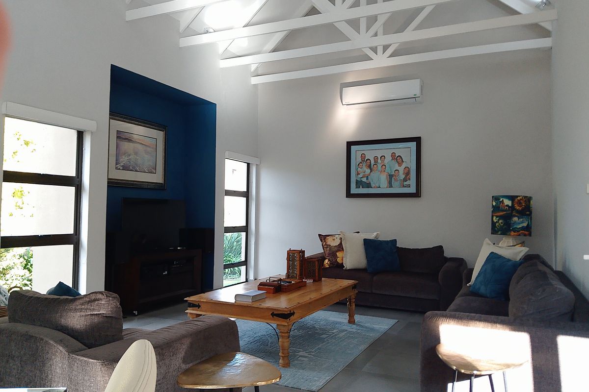 Spacious living room featuring high vaulted ceilings with exposed white trusses, tiled flooring, and a dedicated blue-accented media alcove.