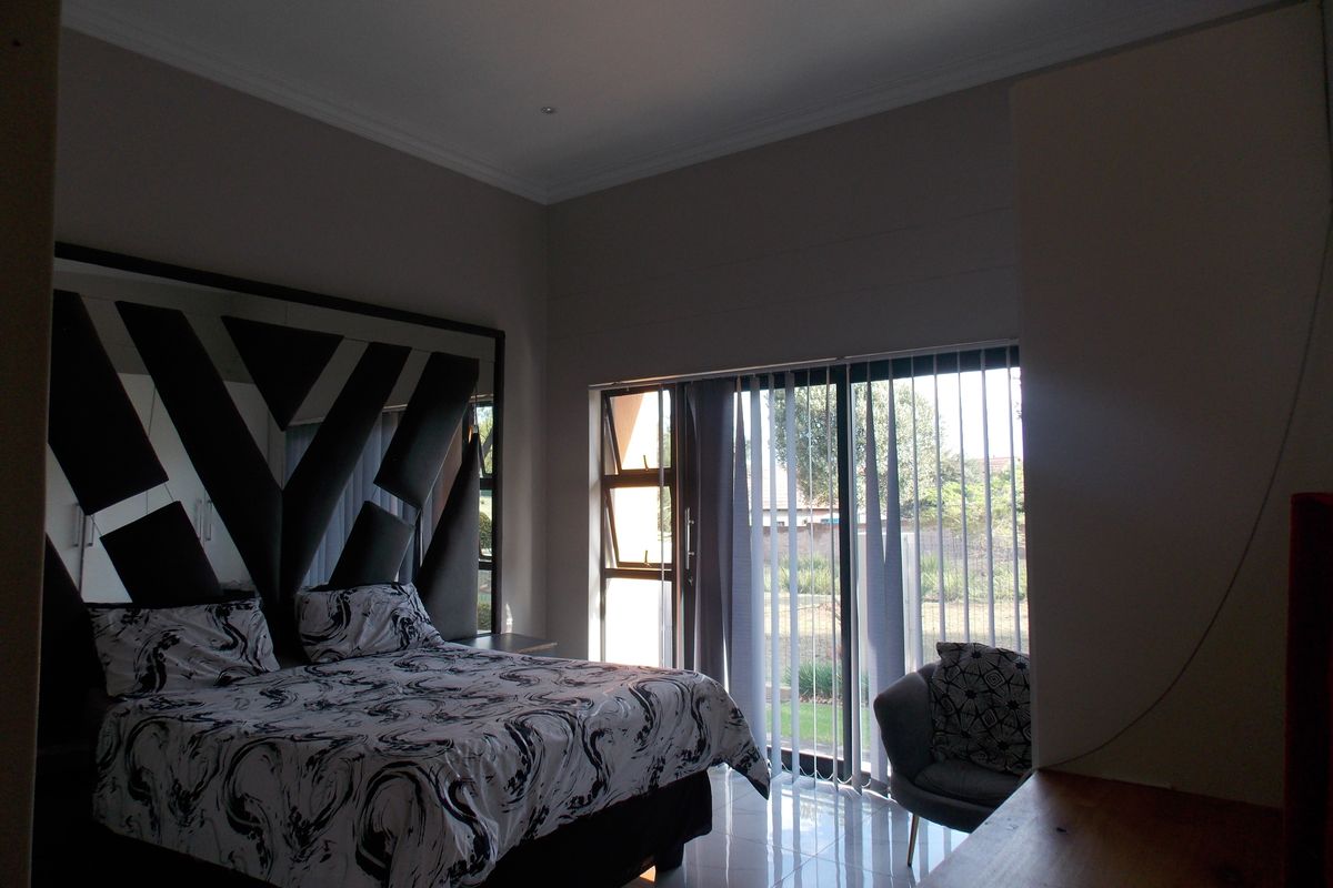 Spacious bedroom featuring tiled flooring, large sliding glass doors with vertical blinds, and a built-in headboard wall feature.