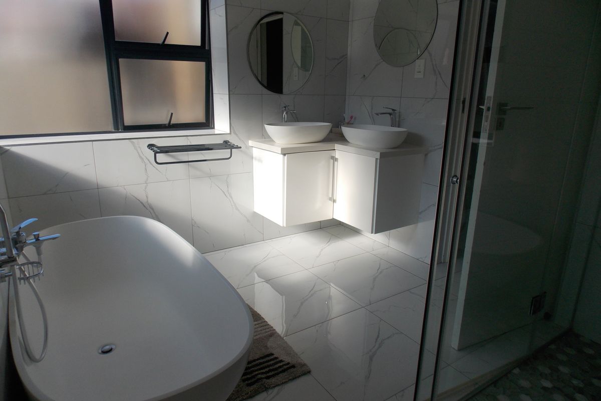 Modern bathroom featuring a freestanding bathtub, double vanity with vessel sinks, and a glass-enclosed shower with marble-look wall and floor tiling.