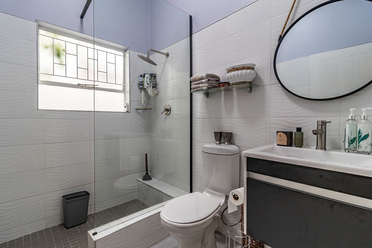 Modern bathroom featuring a walk-in shower with glass screen, wall-mounted vanity, and textured white wall tiles.