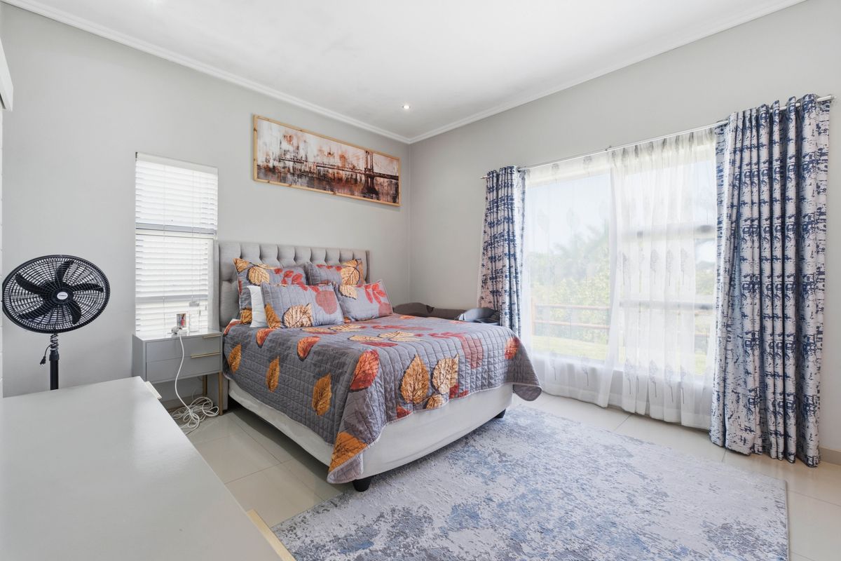 A bright and spacious bedroom featuring large windows with natural light, tiled flooring, and neutral wall finishes.