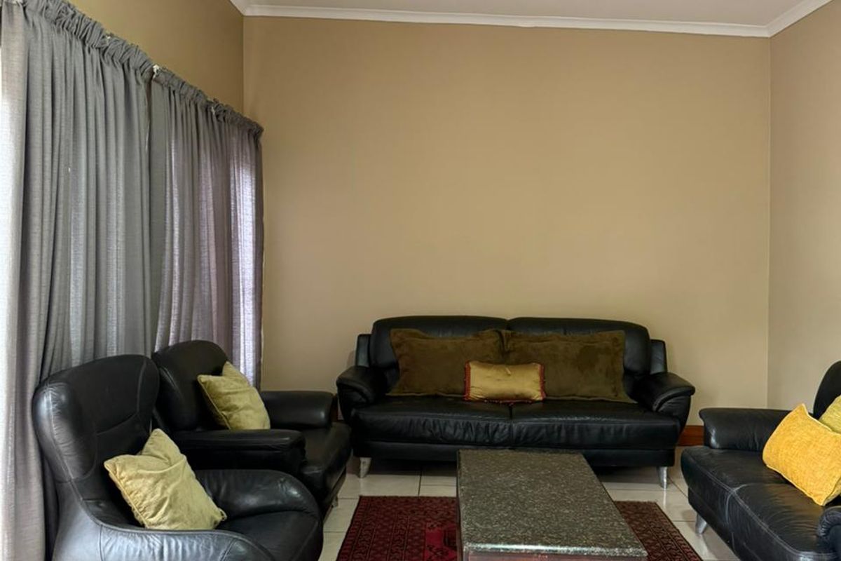 A living room featuring neutral wall tones, tiled flooring, and large windows with curtain tracks.