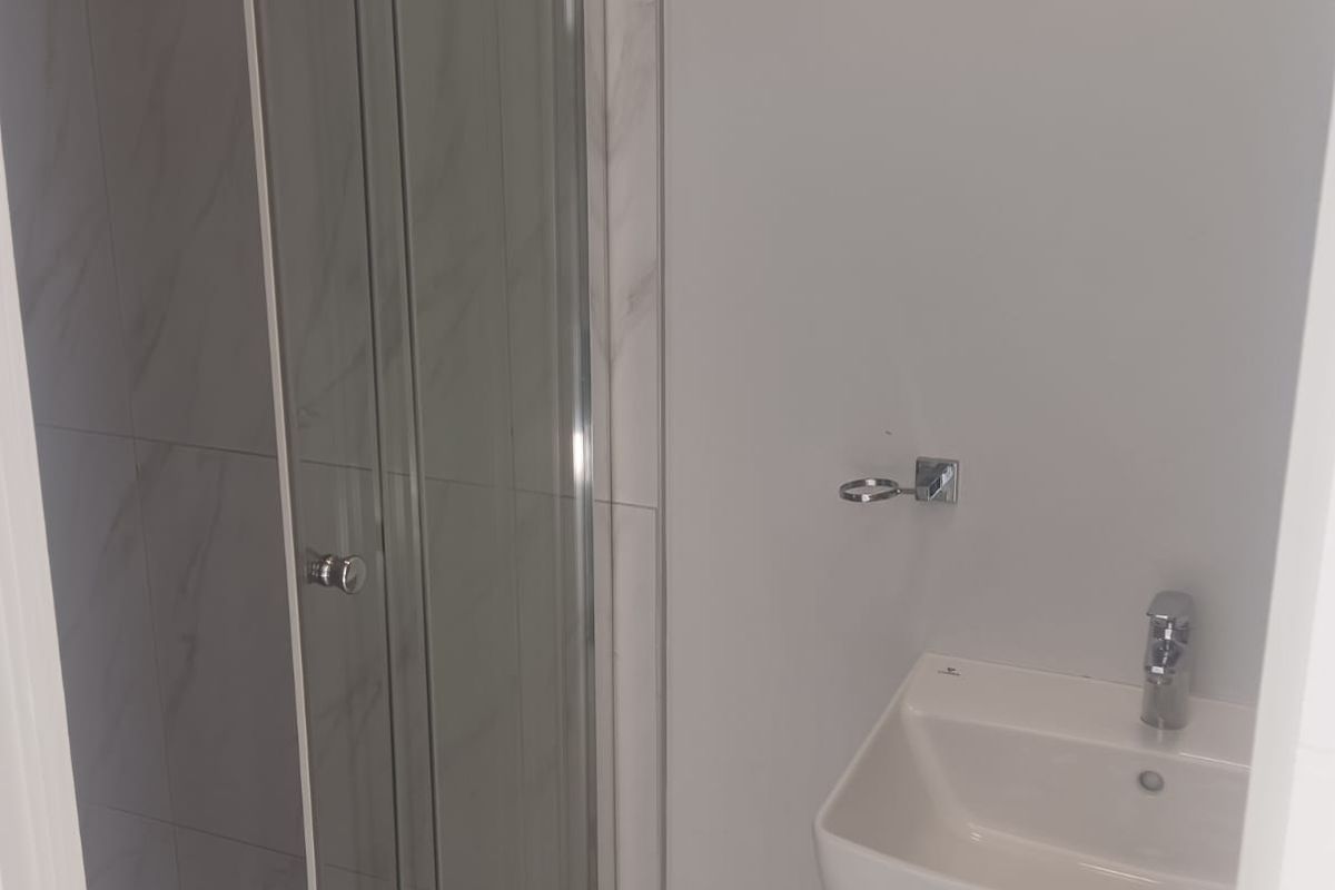 A compact bathroom featuring a modern glass-enclosed shower with marble-look wall tiles and a white pedestal basin.